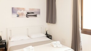 Camera d'albergo con un letto, un comodino, una lampada, un quadro e una finestra con tende.