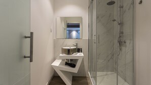 Un baño moderno con cabina de ducha de vidrio, tocador blanco con lavamanos y espejo sobre el tocador.