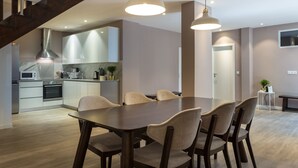 Una cocina moderna con horno empotrado y microondas, un comedor con una mesa grande y sillas, y una escalera que conduce a un nivel superior.