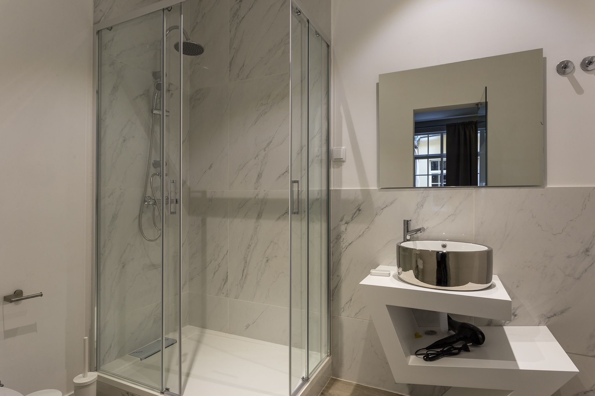 A modern bathroom with a glass-enclosed shower, a white sink with a chrome basin, and a mirror above the sink.