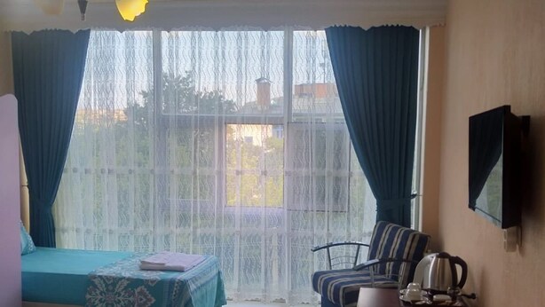 A hotel room with two beds, a desk with a kettle, a chair, and a TV on the wall. - Otel Alimoglu (Gelendost)