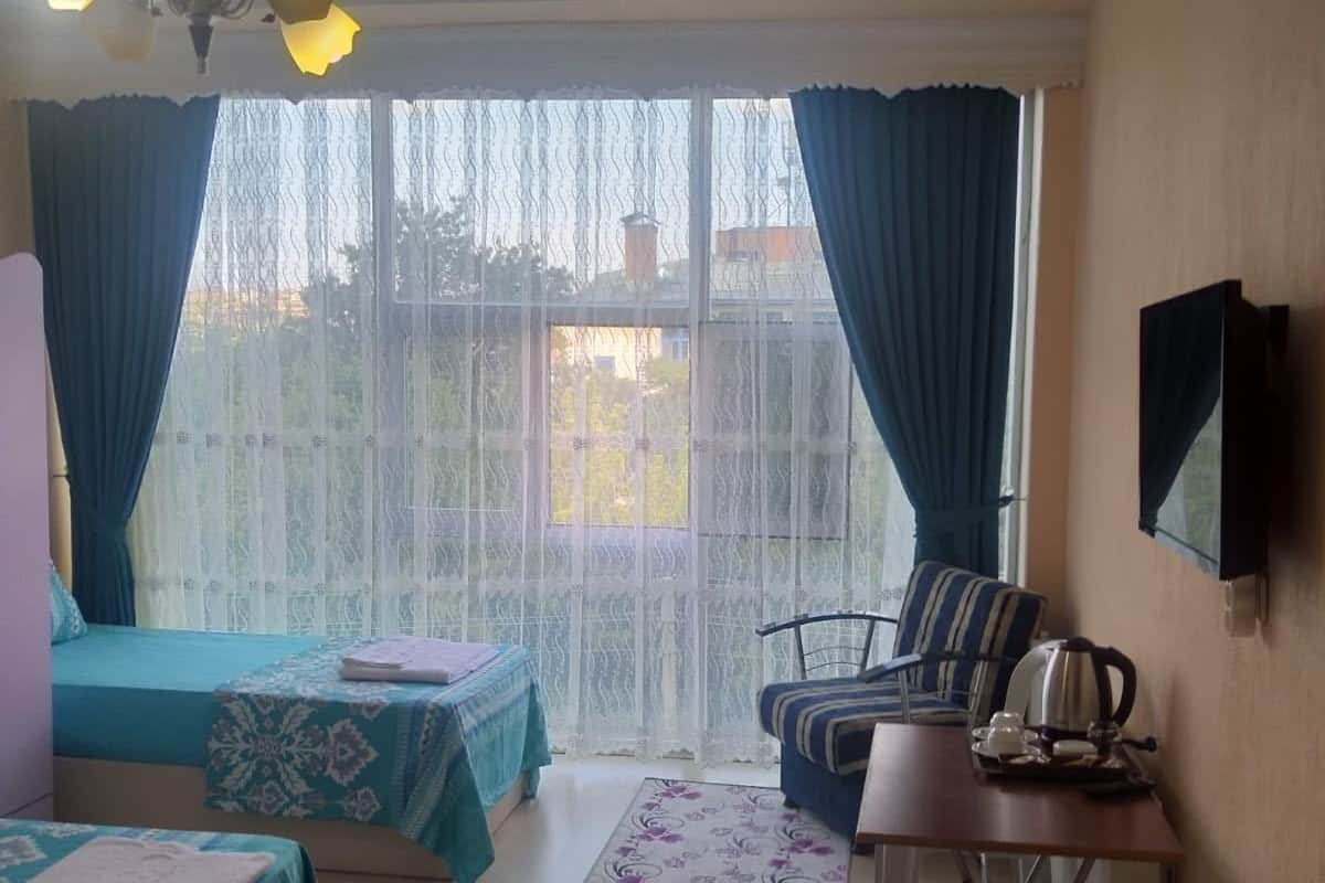 A hotel room with two beds, a desk with a kettle, a chair, and a TV on the wall.