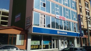 A multi-story hotel with a blue facade, a visible sign for 'Alimoglu Hotel', and a 'Halkbank' bank branch at the ground level. - Otel Alimoglu (Gelendost)