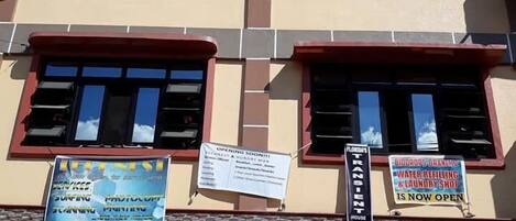 Un edificio a più piani con diversi cartelli pubblicitari che offrono servizi come 'Funniest Surfing' e 'Water Refilling & Laundry Shop'.