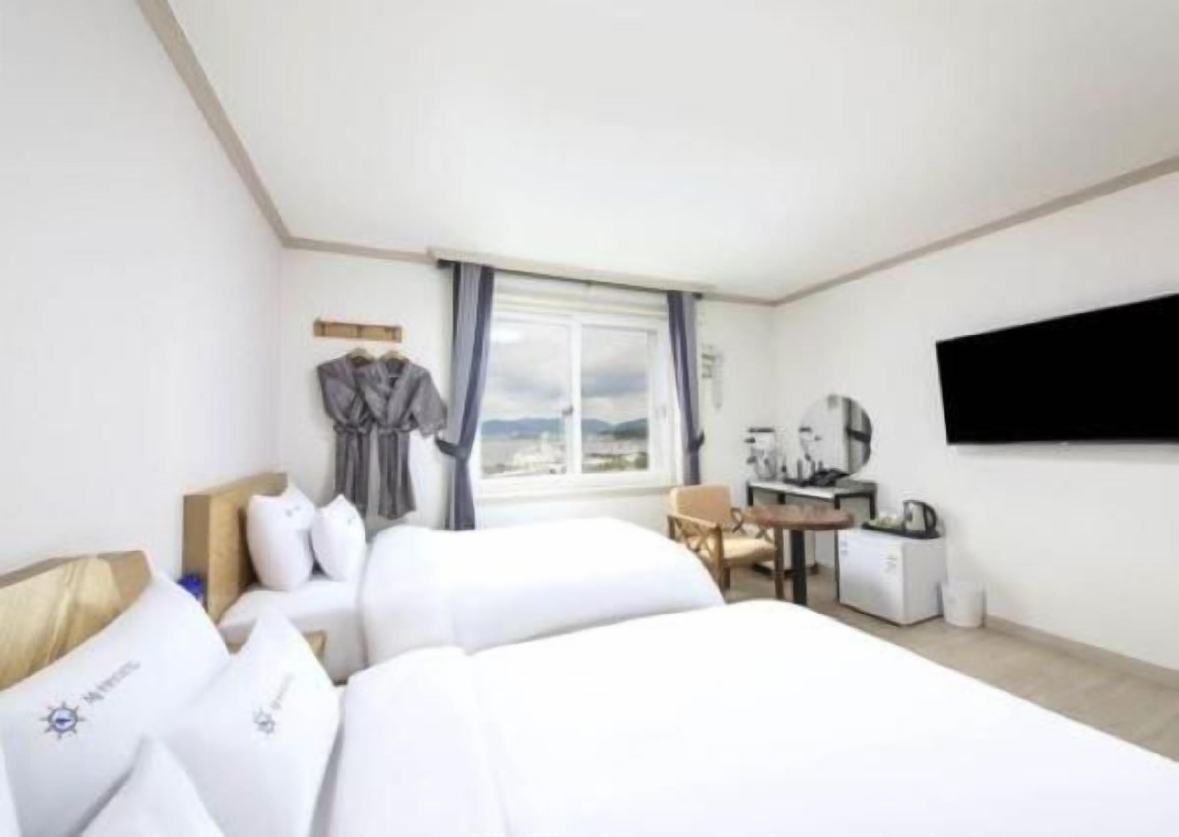 A hotel room with two beds, a desk, a chair, a TV, and a window with a view.