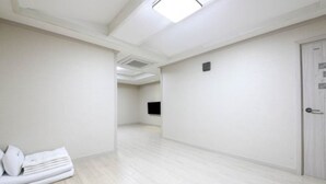 A hotel room with a light wooden floor, a white door, and a flat-screen TV mounted on the wall. - MJ Tour Hostel (Yeosu)