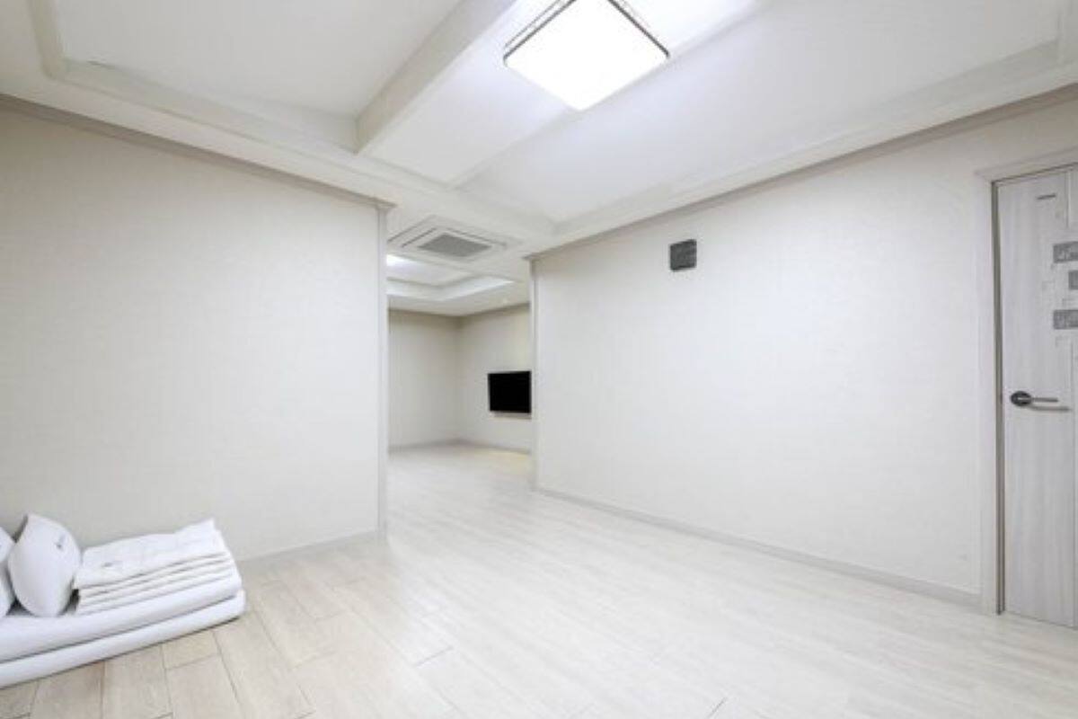 A hotel room with a light wooden floor, a white door, and a flat-screen TV mounted on the wall.