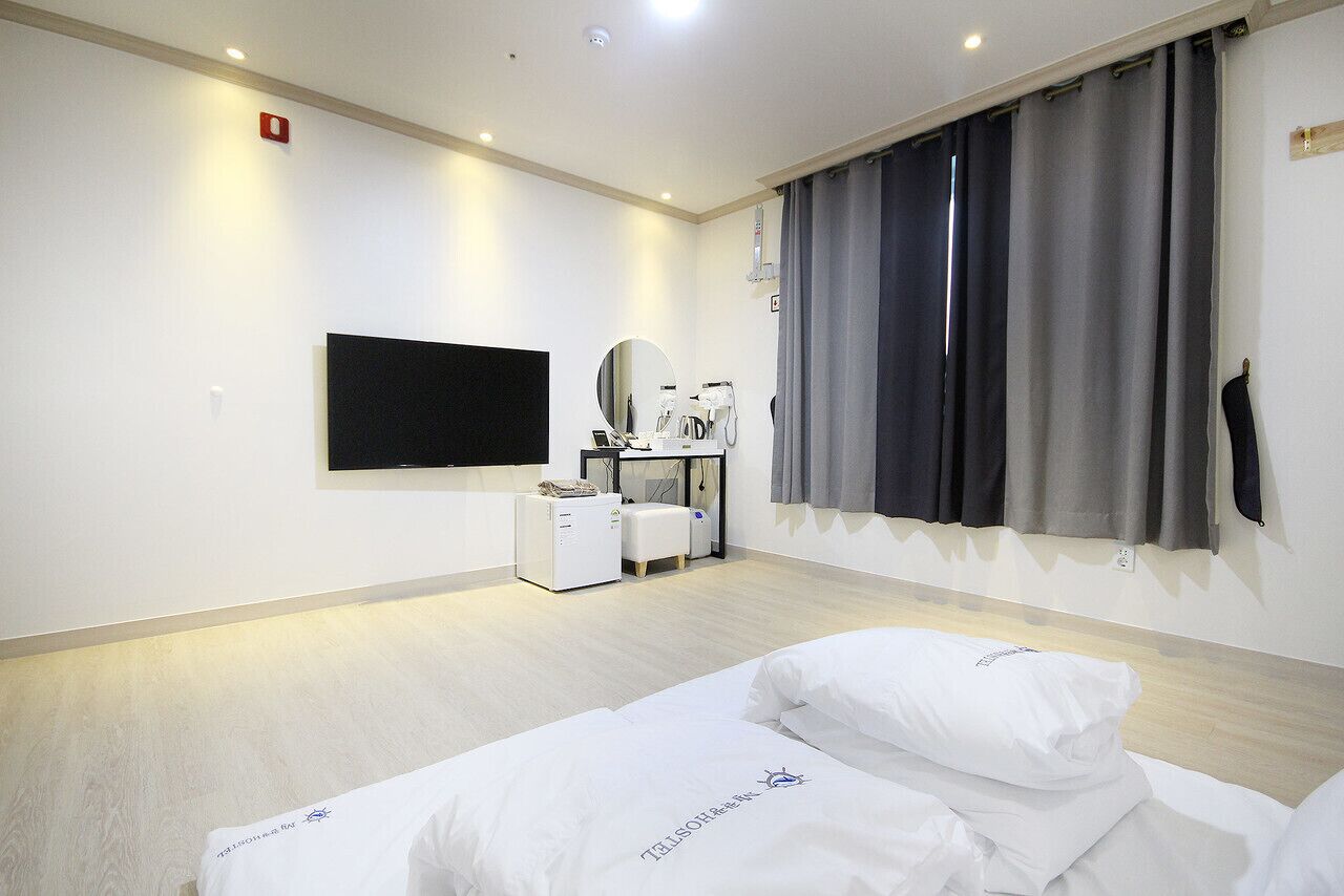 A hotel room with a bed, a TV, a desk with a computer, and a hairdryer.