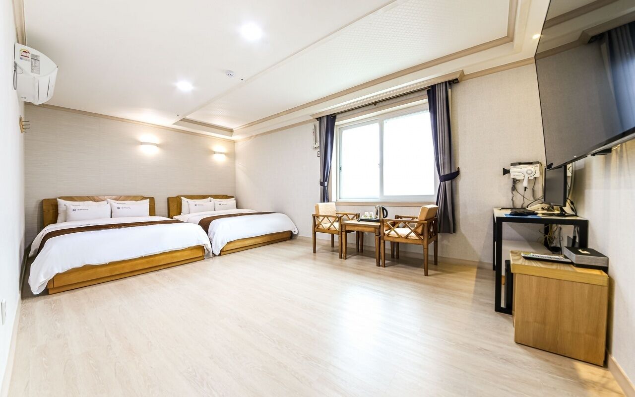 Habitación de hotel con dos camas, un escritorio, una silla, un televisor y una ventana con cortinas.