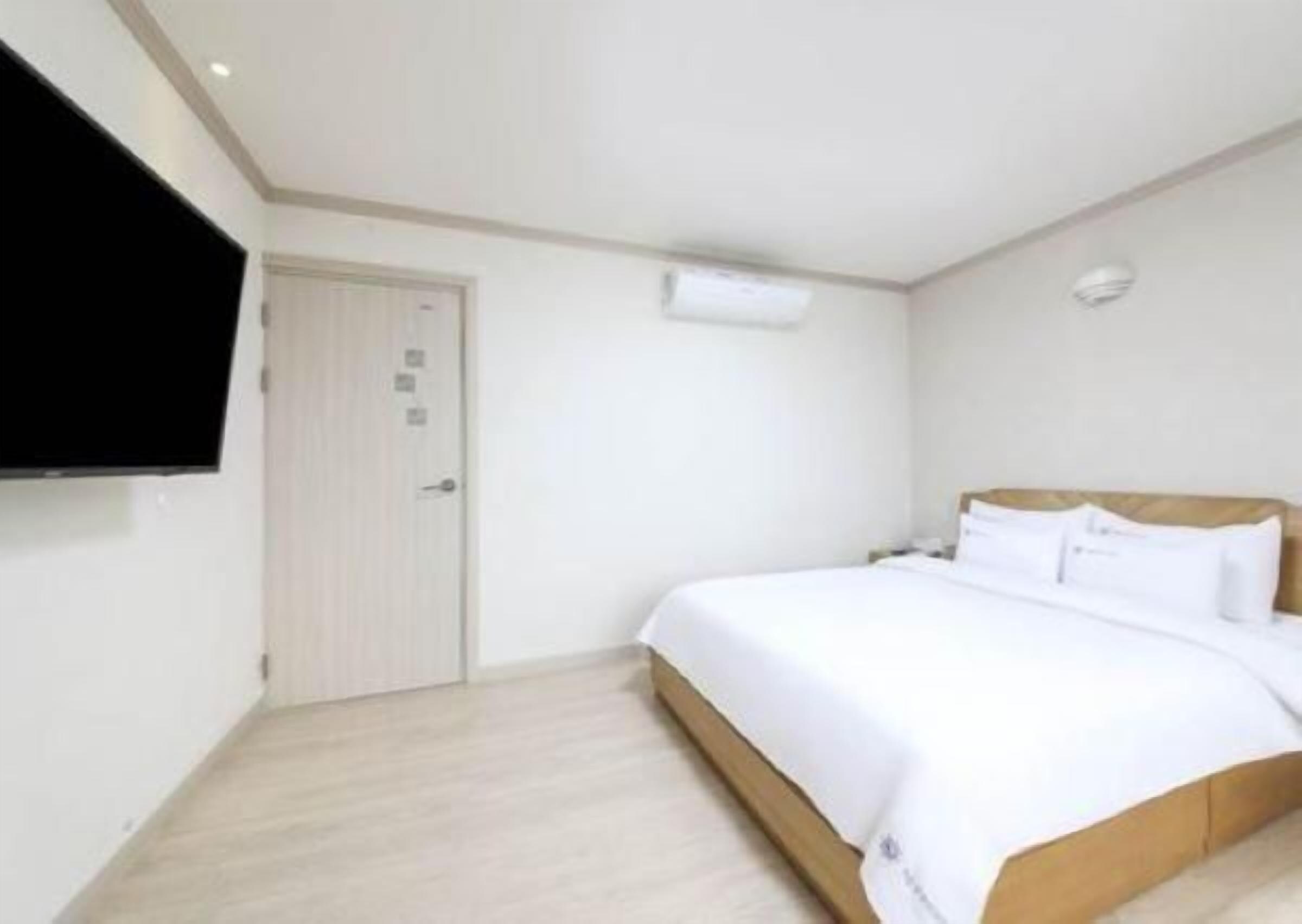 Un dormitorio con cama, puerta y televisión instalada en la pared.