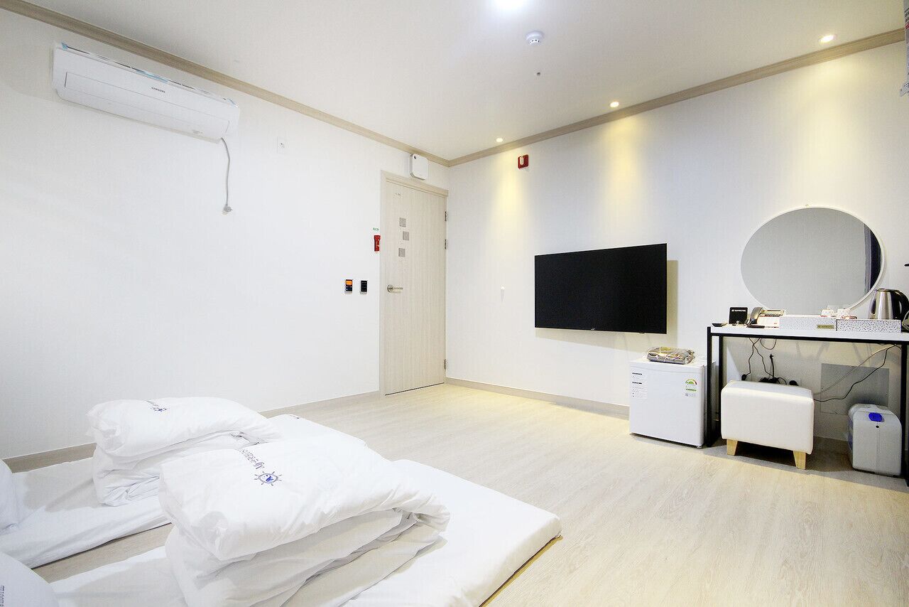 Une chambre d’hôtel avec un lit, une télévision, un bureau avec un ordinateur et une petite armoire blanche.