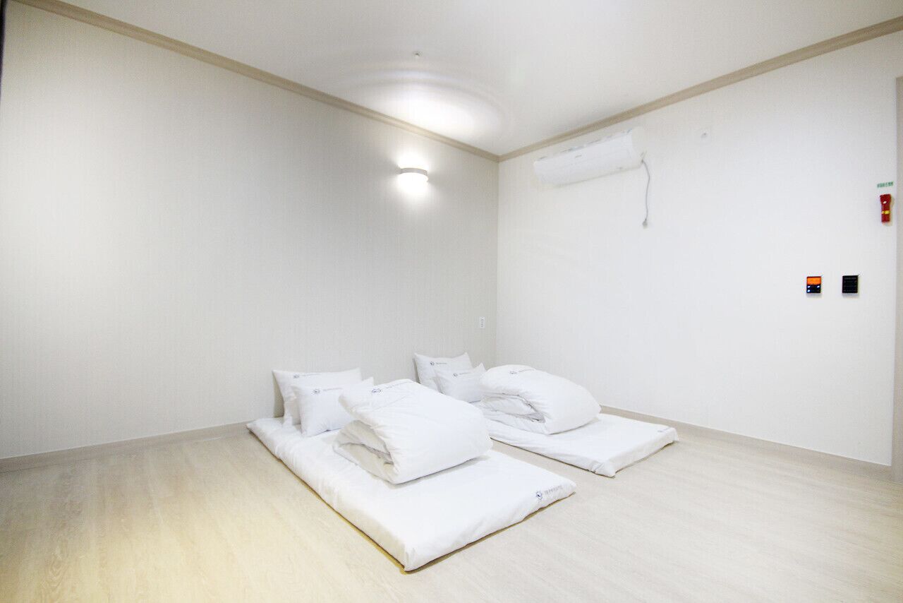 Une chambre d’hôtel avec deux lits, du linge de lit blanc, un plancher en bois, un luminaire au plafond et un climatiseur fixé au mur.
