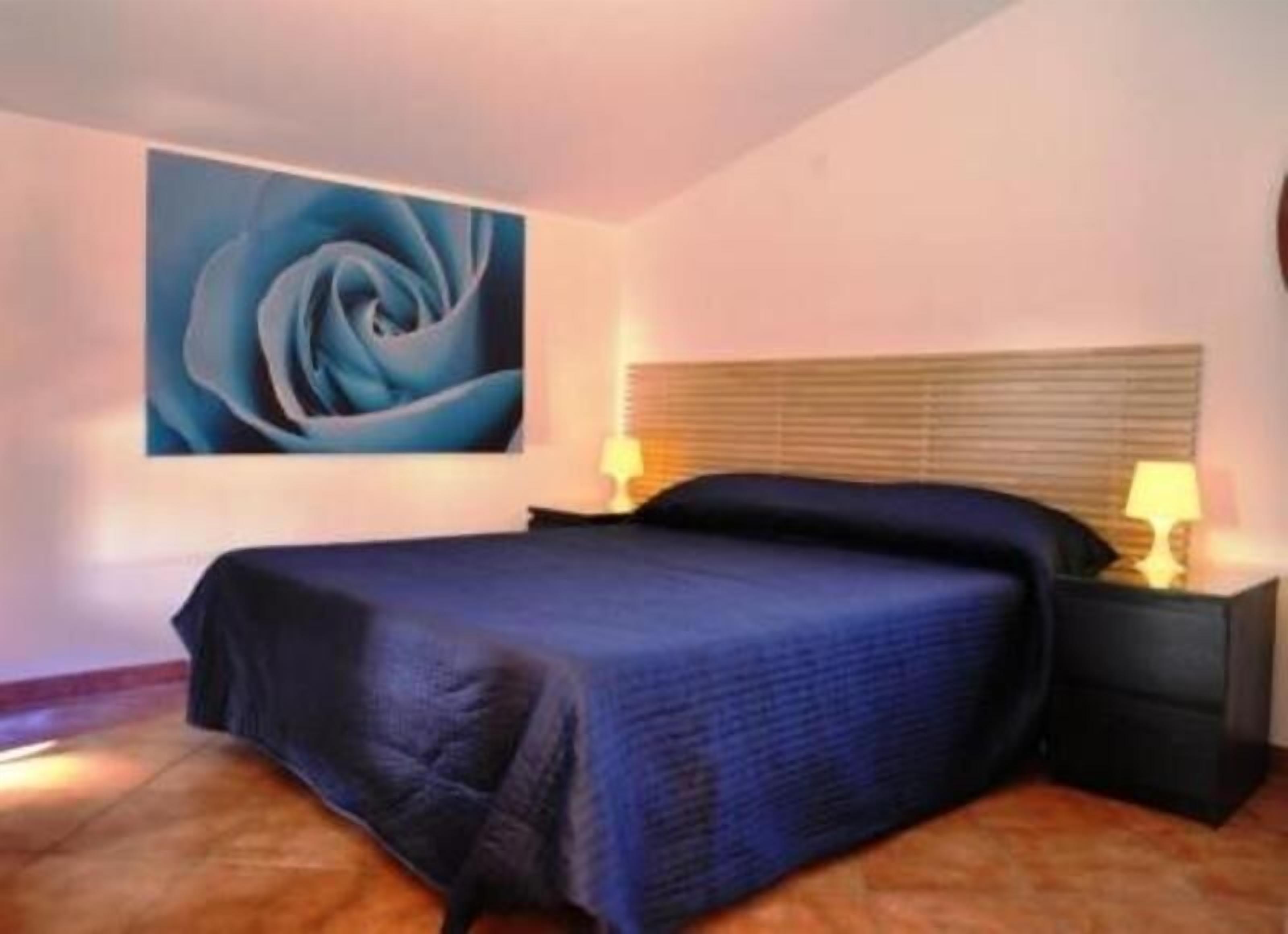 A bedroom with a large bed, a nightstand with a lamp, and a wall-mounted painting.
