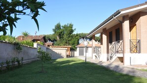 Une cour avec une petite pelouse, un bâtiment en briques doté d’un patio couvert et un portail en métal.