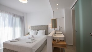 A modern hotel room with a large bed, a bedside table with a lamp, a bathroom with a sink and mirror, and a view of the city.