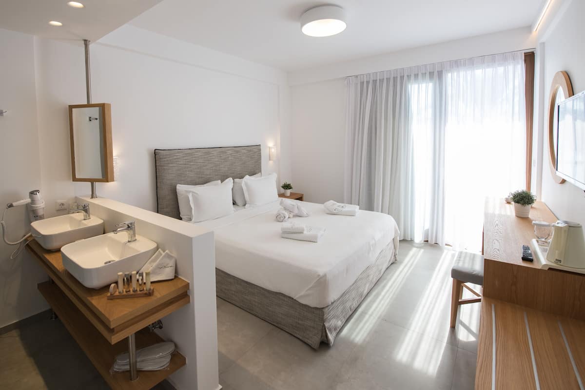 Une chambre d’hôtel moderne avec un grand lit, deux tables de chevet, un lavabo intégré et un miroir.