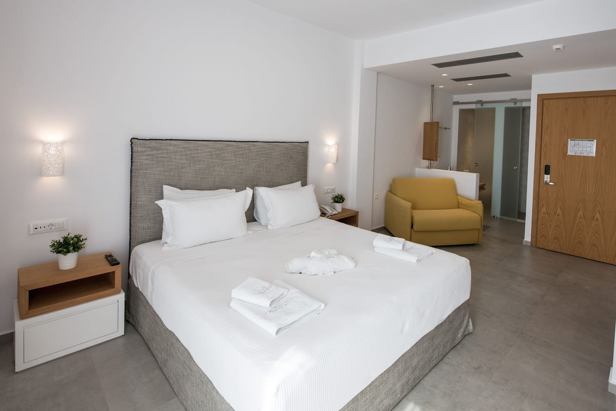 Une chambre d’hôtel moderne avec un grand lit, une table de chevet avec une lampe, une chaise et une armoire.