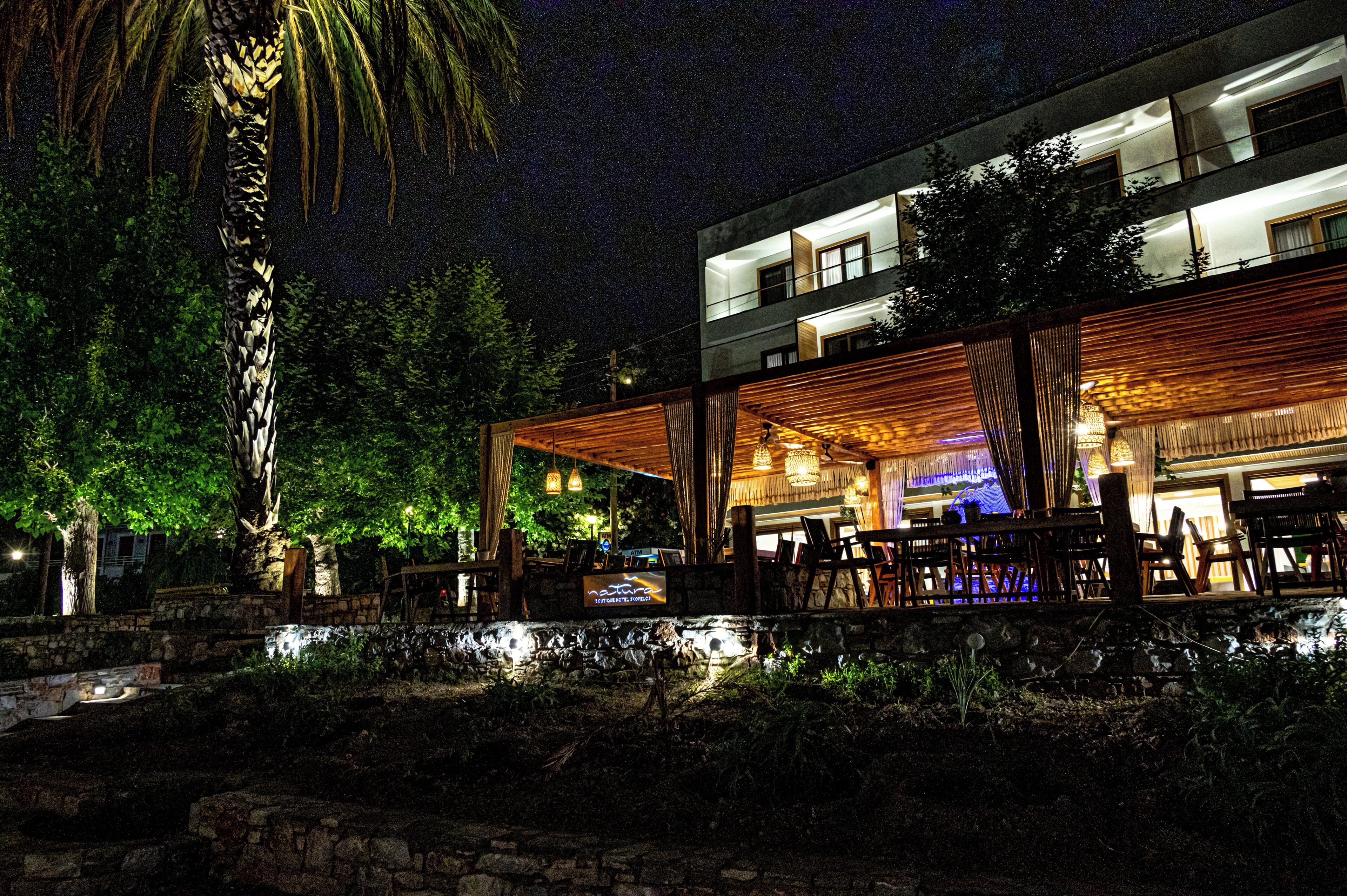 A modern building with a covered outdoor seating area, stone walls, and a palm tree.