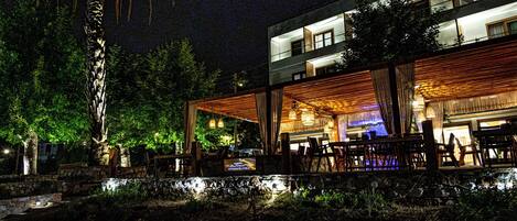 A modern building with a covered outdoor seating area, stone walls, and a palm tree.