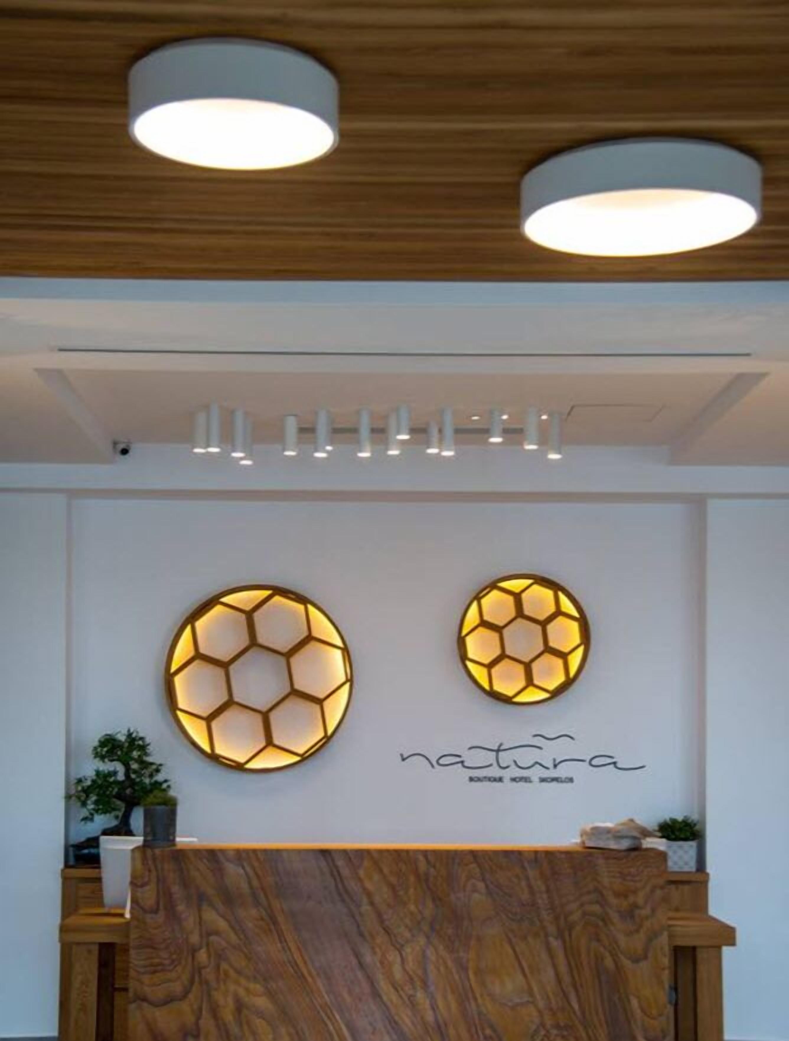 Un mostrador de recepción con acabado de madera, dos piezas de arte mural iluminadas con patrones hexagonales y un techo con iluminación empotrada.