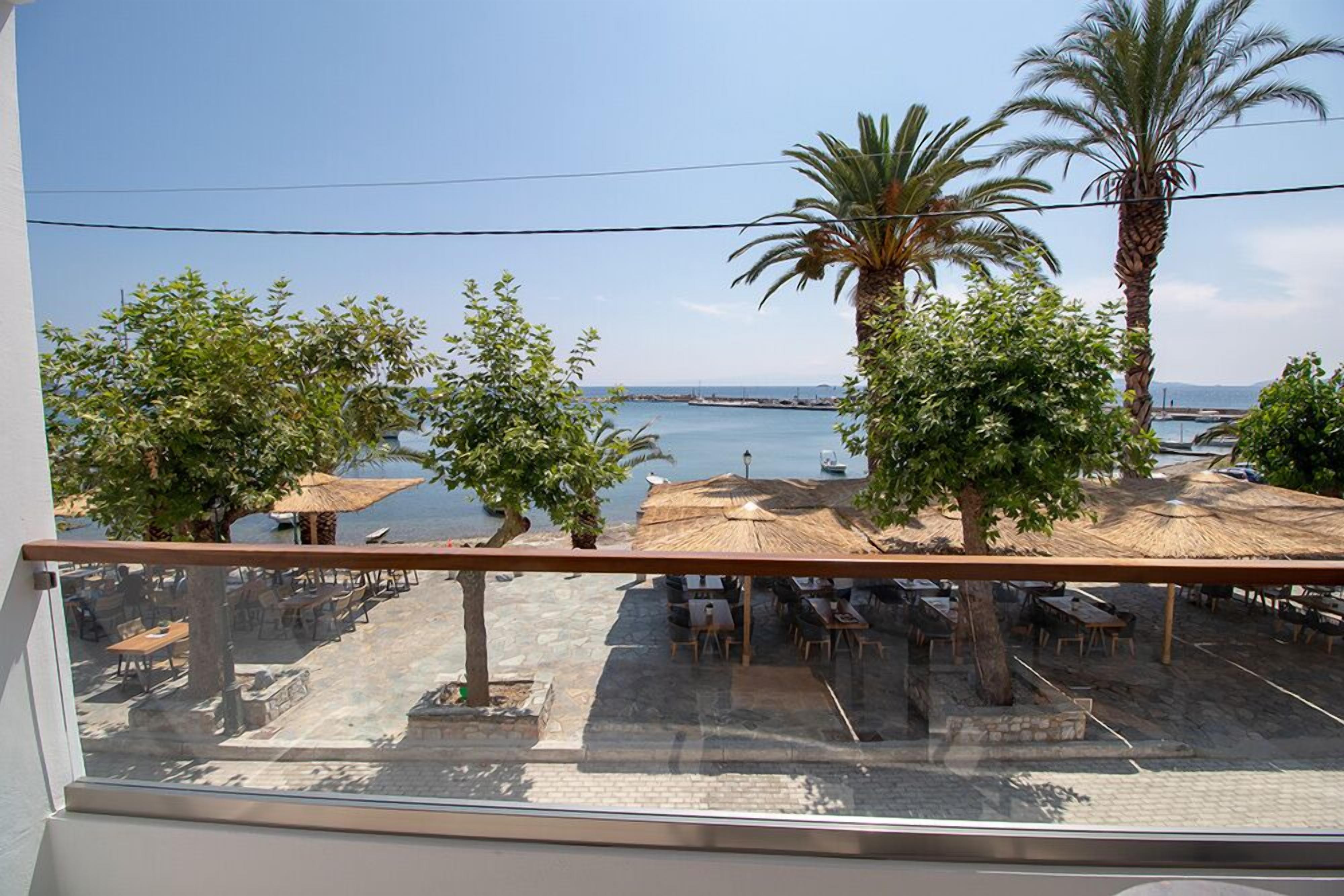 Un balcón con vista a una playa, palmeras y mobiliario exterior.