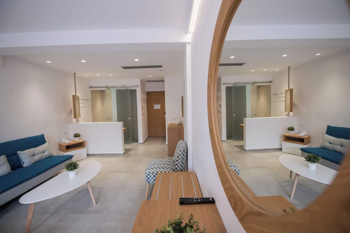 Un salon moderne avec un canapé, une table basse, un pouf à motifs et un miroir qui reflète la pièce.