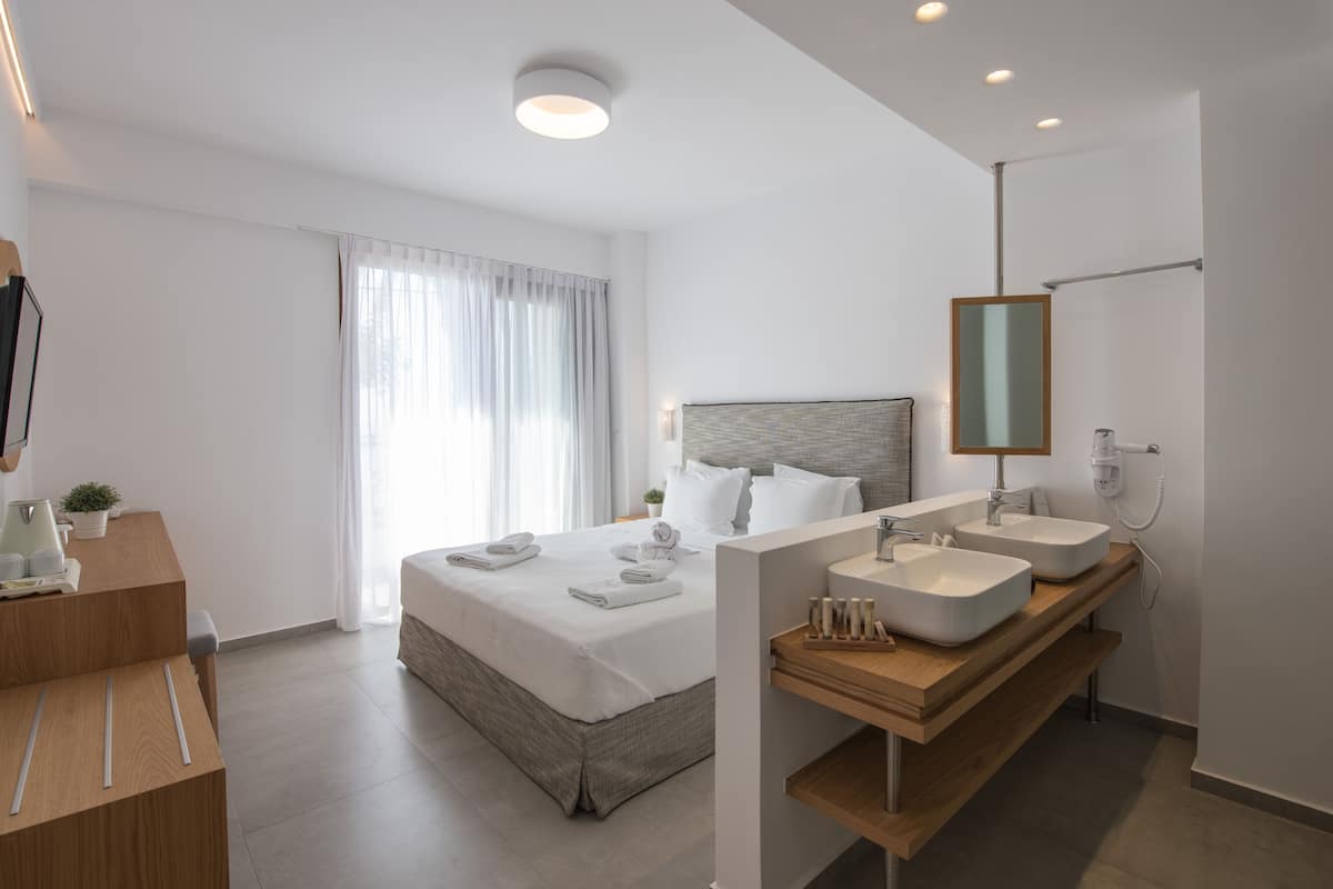 Une chambre d’hôtel moderne avec un grand lit, une coiffeuse en bois dotée de deux vasques, un miroir et un sèche-cheveux.