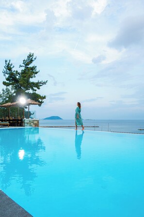 A woman in a blue dress walking along the edge of a pool with a view of the sea and a distant island. - Natura Luxury Boutique Hotel Skopelos (Skopelos)