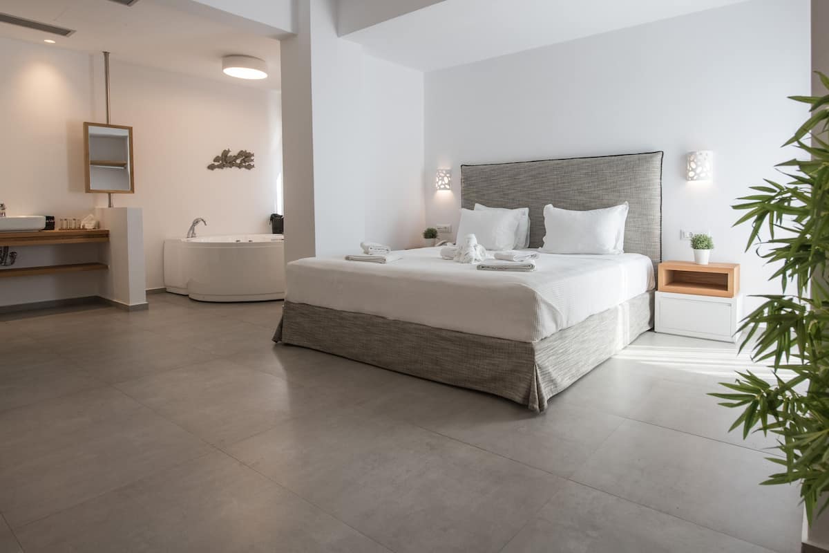Une chambre à coucher moderne avec un grand lit, une baignoire intégrée et une table de chevet agrémentée d’une plante.
