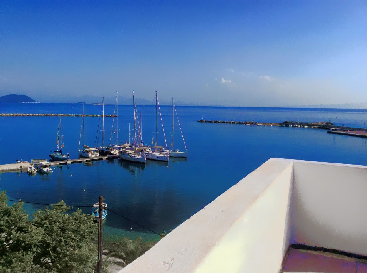 A marina with several sailboats docked, a clear blue sky, and a distant mountain range.