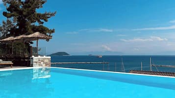 A clear blue pool with a stone structure and lounge chairs on one side, overlooking a calm sea and distant islands.