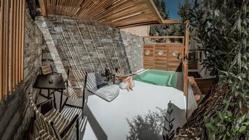 Un área de piscina privada al aire libre con paredes de piedra, asientos de madera y una pequeña mesa.