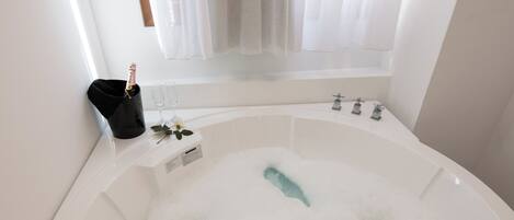 A large, white bathtub filled with bubbles, a champagne bottle, and two glasses on a tray.