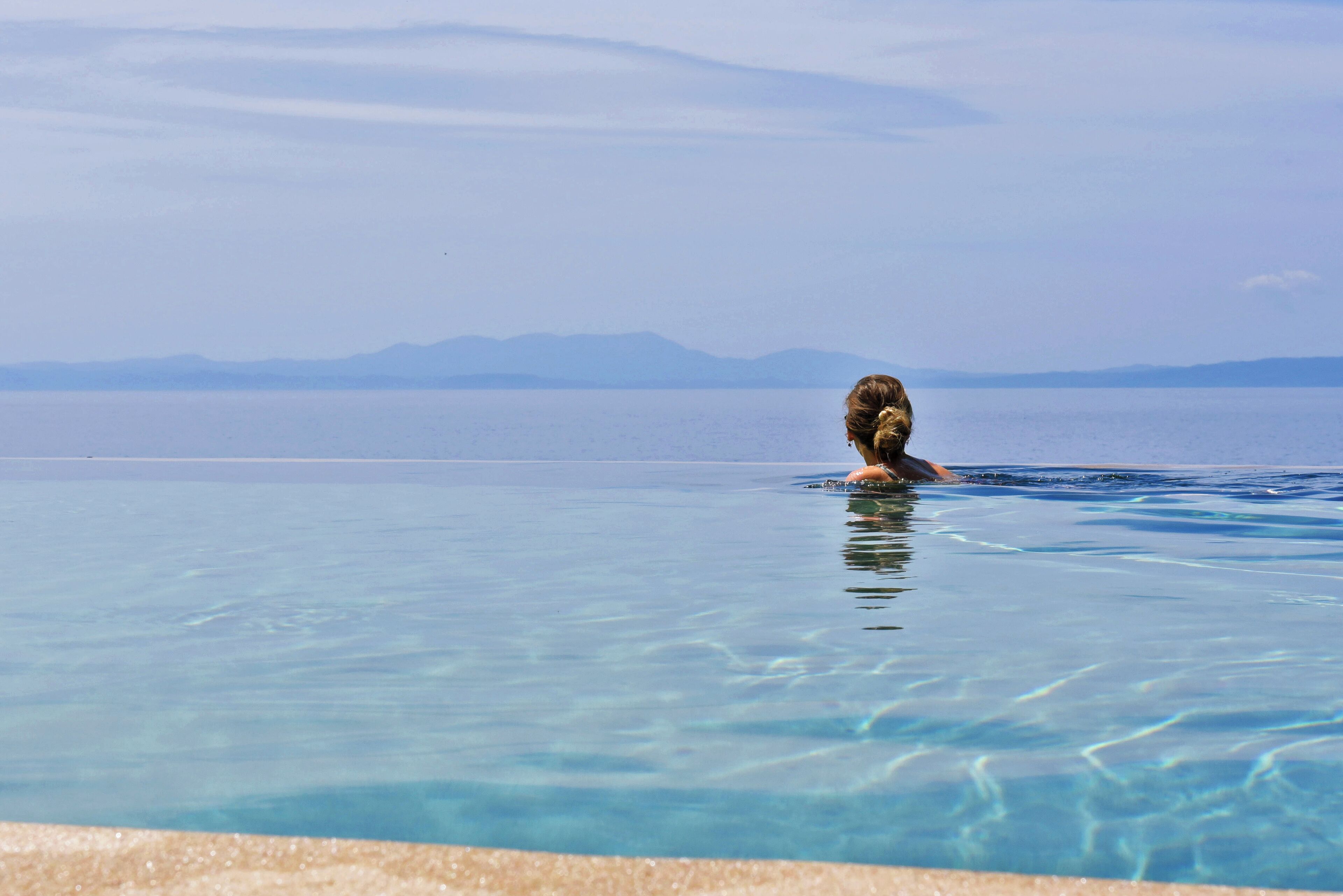 A person in a clear blue pool with a mountainous view in the background.