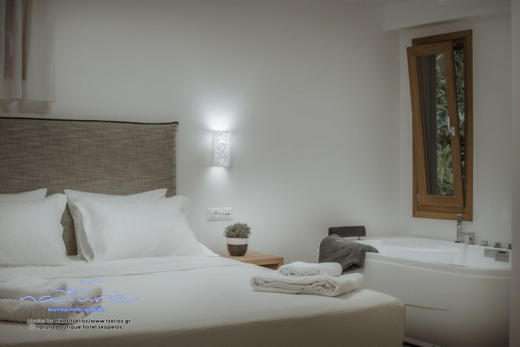 A hotel room with a bed, a nightstand with a lamp, a potted plant, and a bathroom with a bathtub and sink.