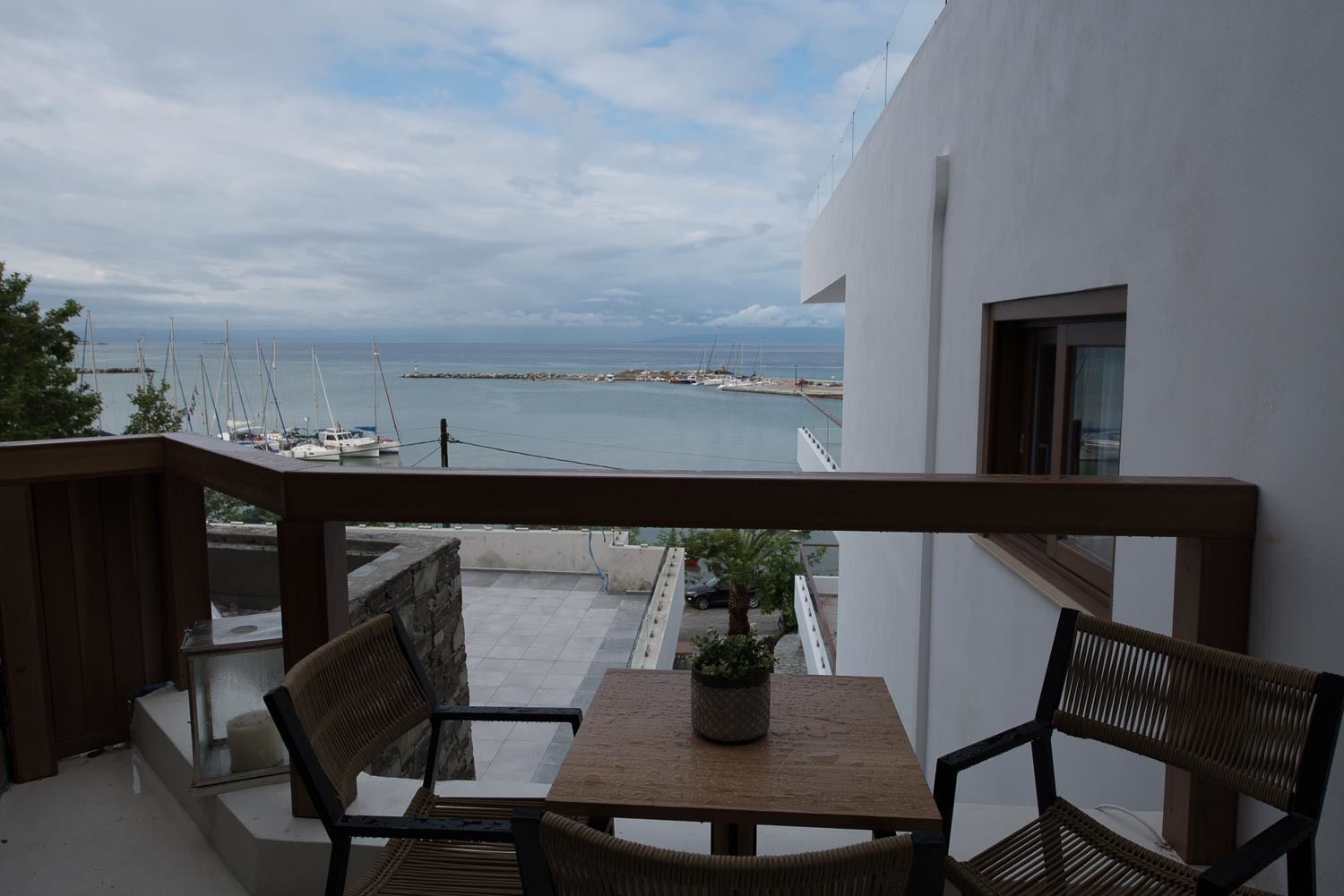 Un balcon avec vue sur la mer, une table, deux chaises et une plante en pot.