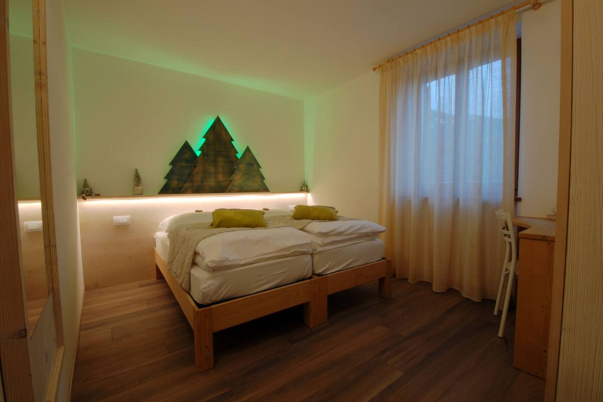 A bedroom with a wooden bed, a nightstand, a desk, and a wall-mounted lamp.