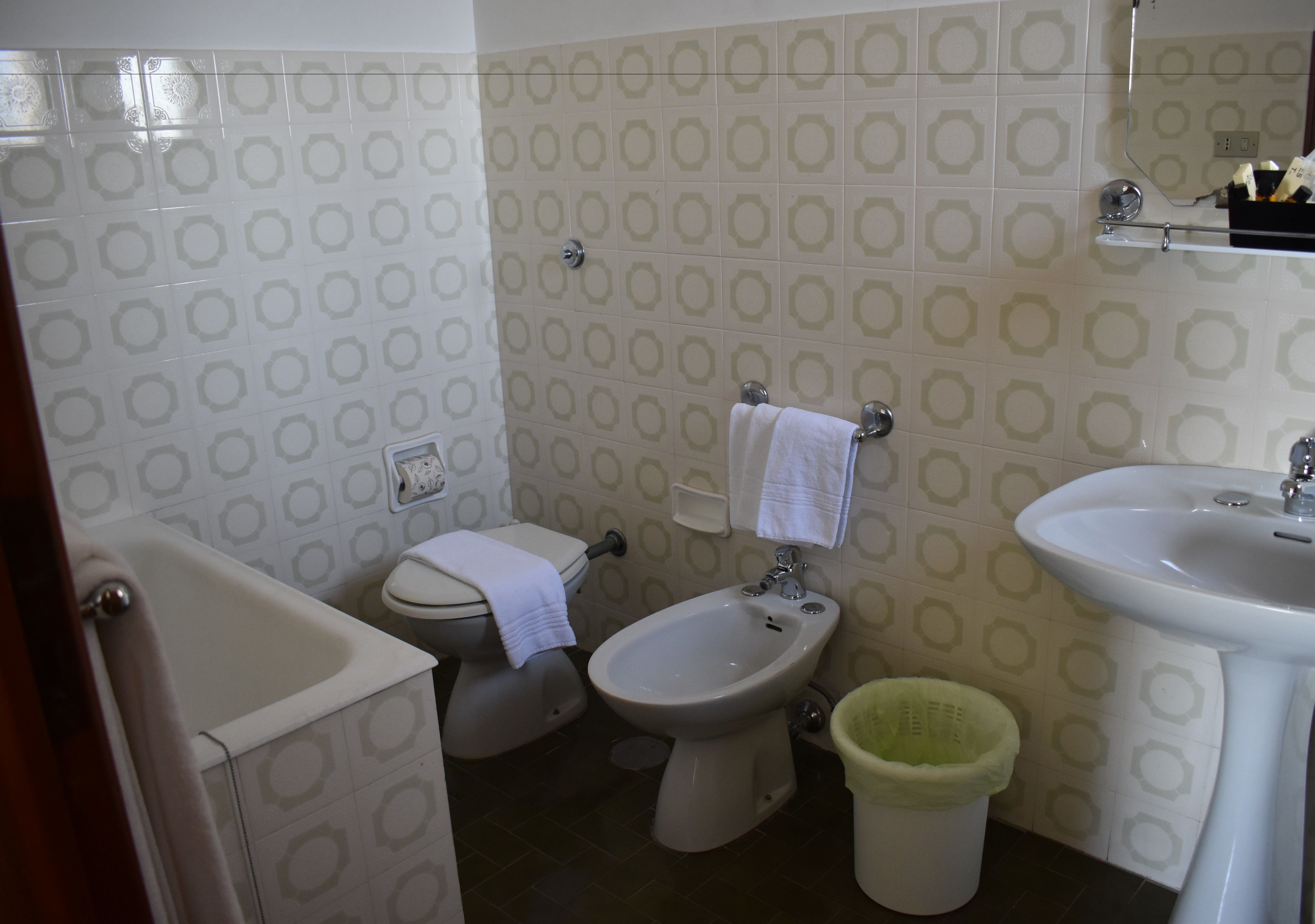 A bathroom with a toilet, bidet, sink, and a green trash bin.