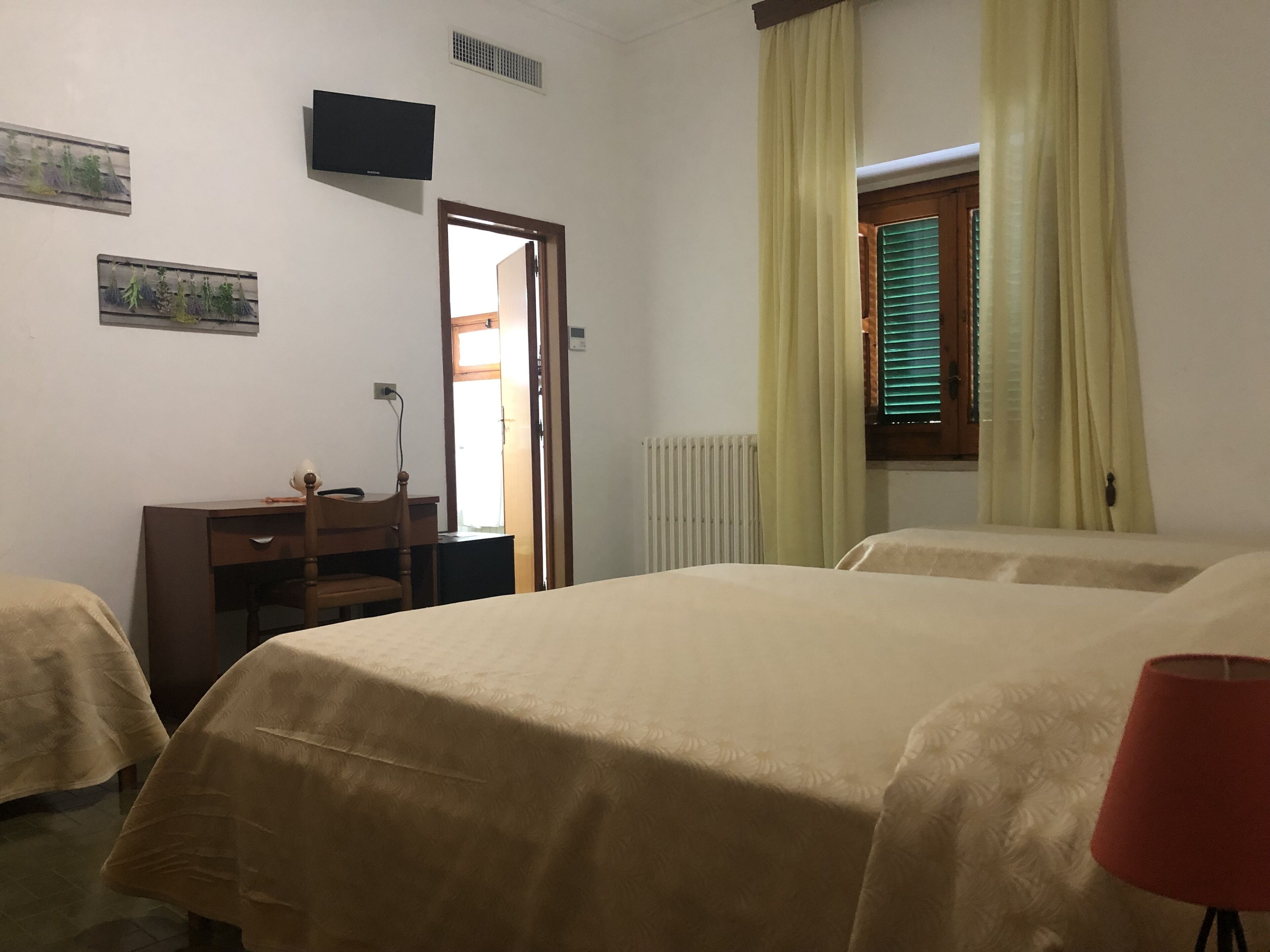 A hotel room with two beds, a desk, a chair, a TV, and a window with curtains.