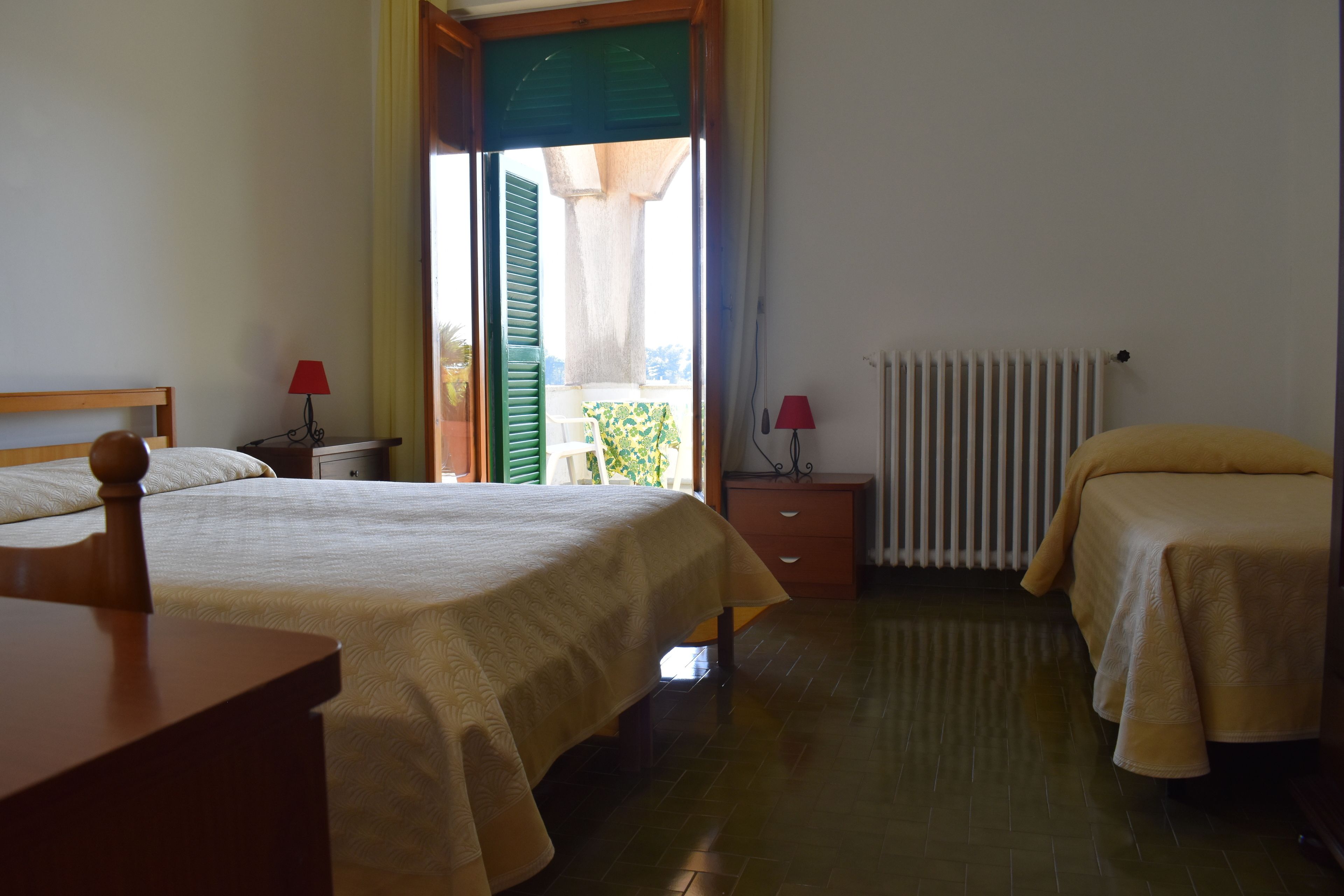 Une chambre à coucher avec un lit, deux tables de chevet, un radiateur et une fenêtre avec des volets.