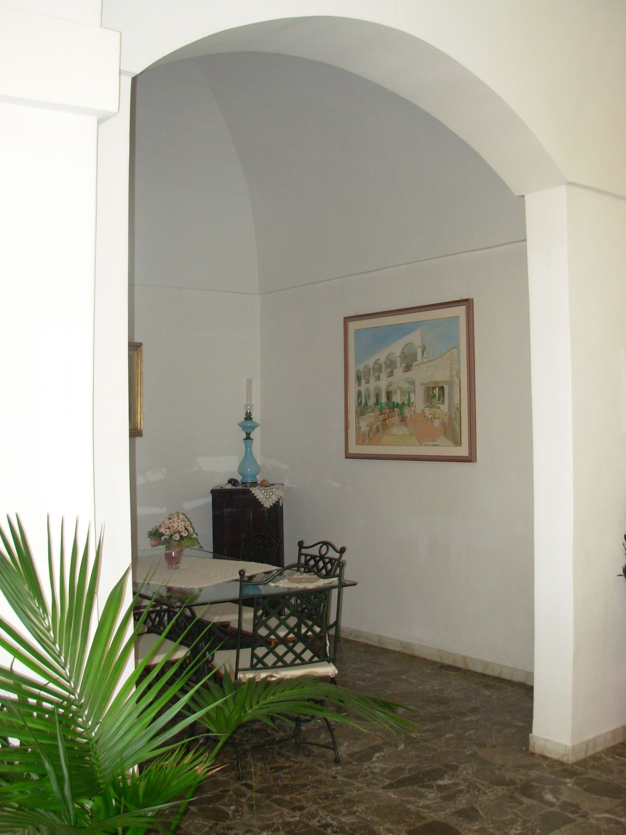 Un comedor con una mesa y sillas, un florero con flores, una lámpara y un cuadro en la pared.