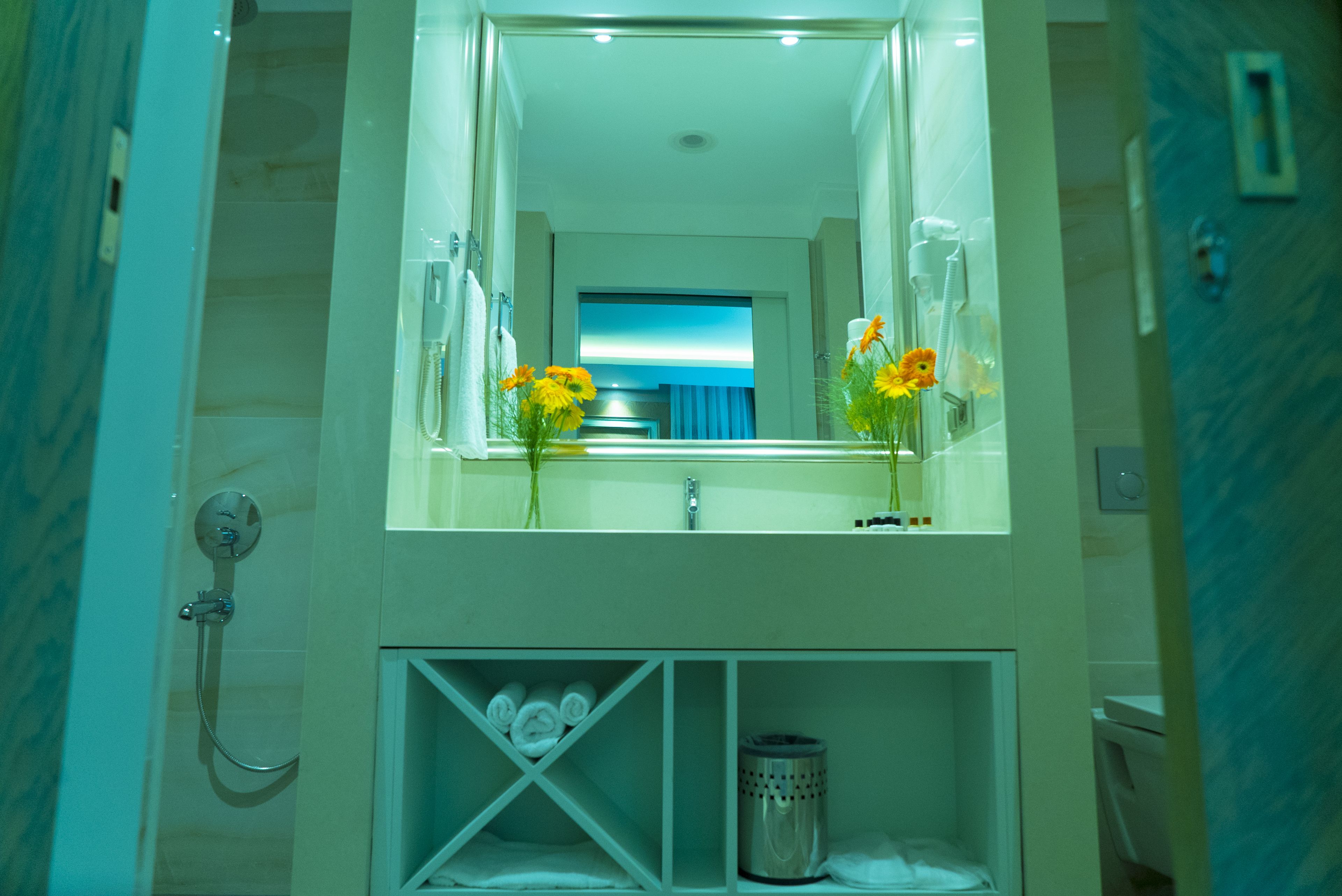 Baño con un espejo grande, ducha e lavamanos. Se ven toallas y artículos de aseo.
