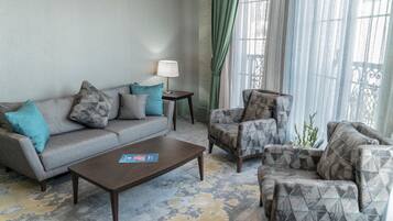 Sala de estar con sofá, sillón y mesa de centro. Una lámpara sobre una mesita auxiliar y una ventana con cortinas.