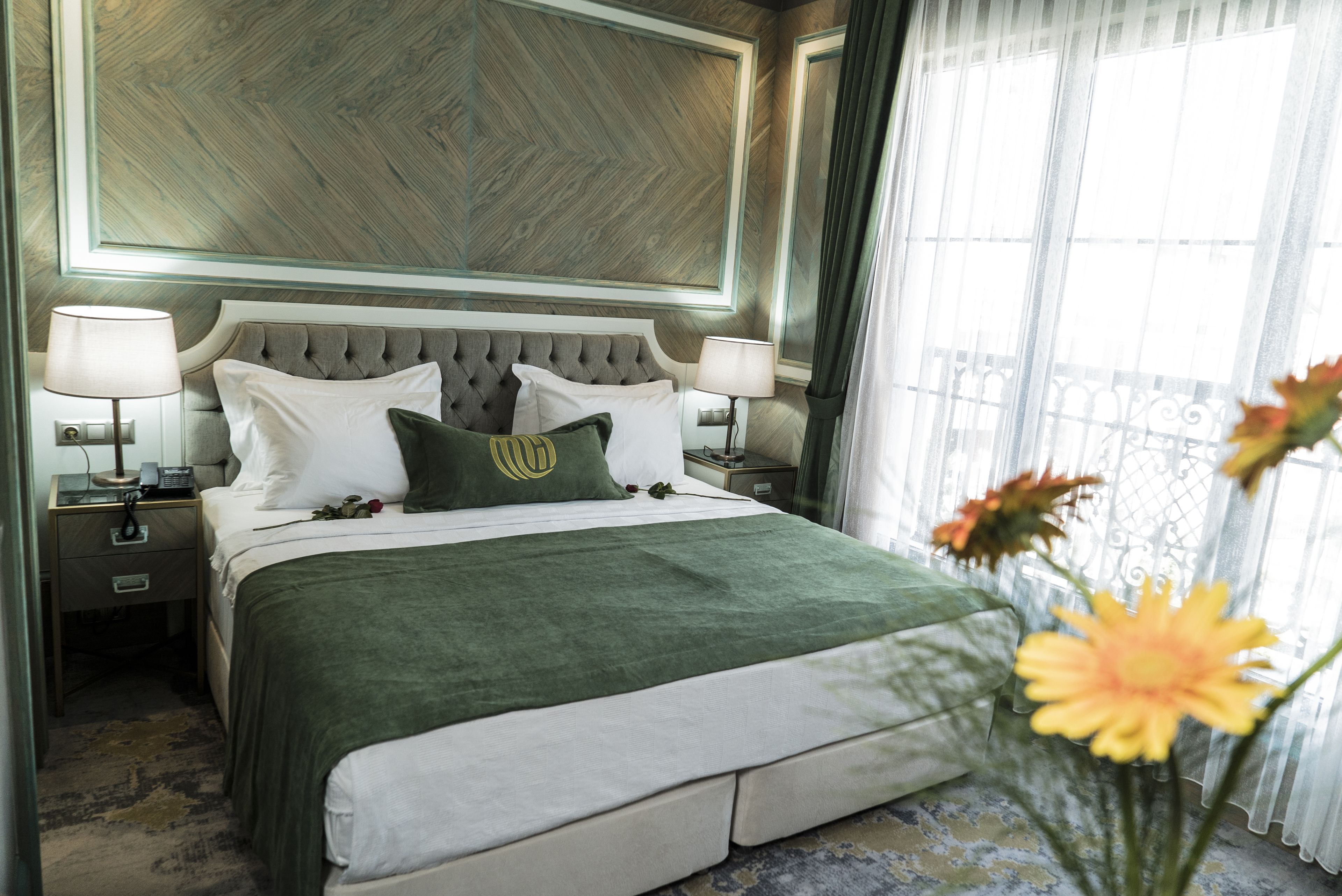 Habitación de hotel con una cama grande, dos mesitas de noche, una manta verde y vistas al exterior a través de una ventana.