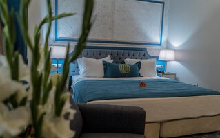 Una cama bien tendida con colcha azul y blanca, cabecera capitonada y una única almohada decorativa con un logotipo.