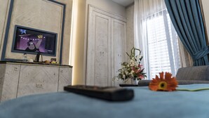 A hotel room with a TV on the wall, a bed with a remote control, a flower on the bed, and a window with curtains. - Mirart Hotel Boutique & SPA Yalova (Yalova)