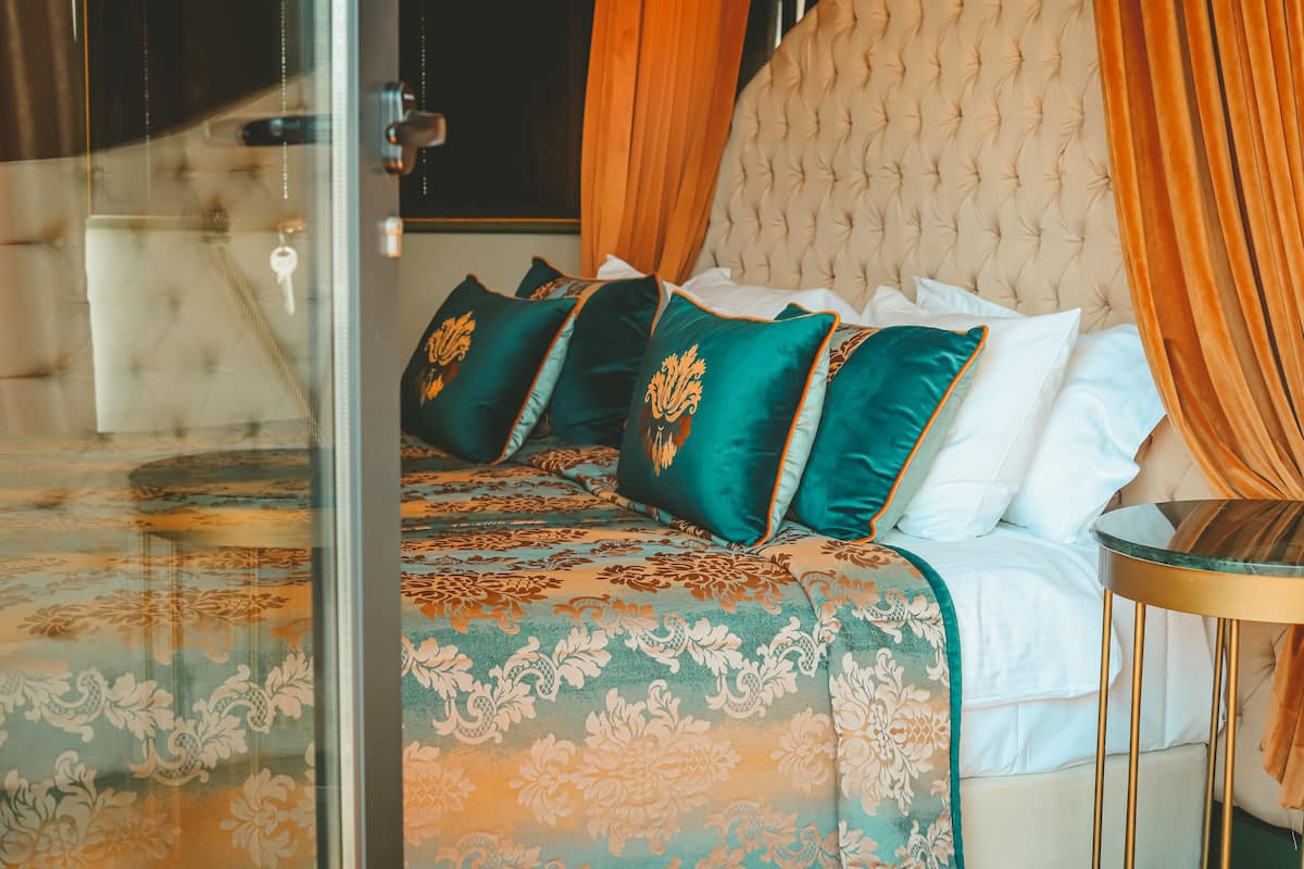 Une chambre à coucher avec une tête de lit capitonnée, un lit agrémenté d’oreillers verts et blancs, et une cloison en verre.