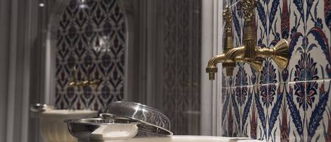 Une salle de bain équipée d’un lavabo, d’un robinet et d’un revêtement mural décoratif en carreaux.
