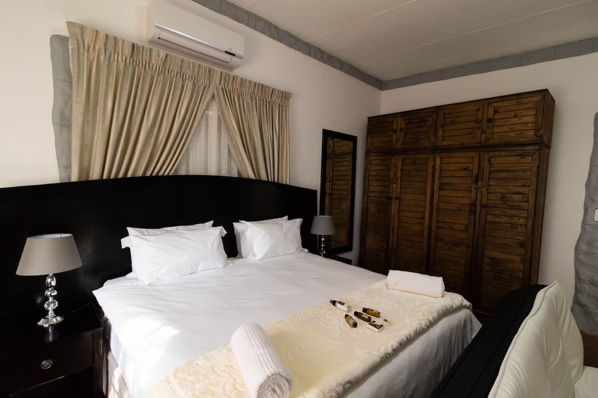 Habitación de hotel con una cama grande, un armario de madera, un equipo de aire acondicionado y una mesita de noche con lámpara.