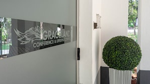 A conference center sign with a logo and text, a door, and a potted plant. - Graceland Conference & Lifestyle Centre (Akasia)